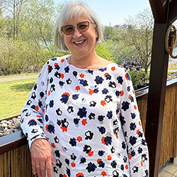 Ältere Dame mit Brille lächelt im Freien. Weißes Shirt mit bunten Blumen. Außenszene.
